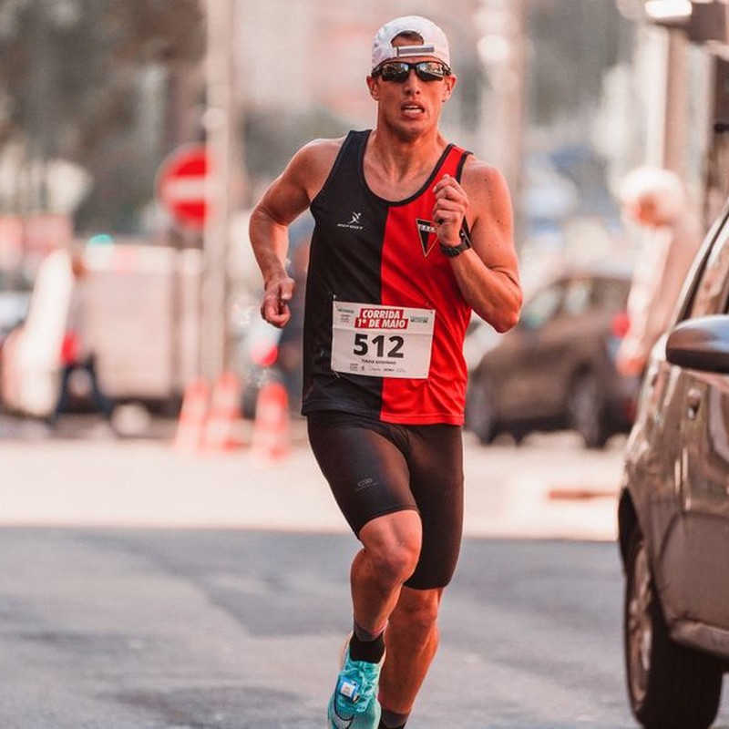 Athletic man wearing a cap and sunglasses competing in a marathon on urban streets.