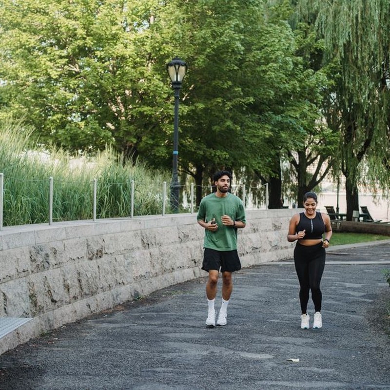 A man and woman jogging together in a lush, green park during the day.