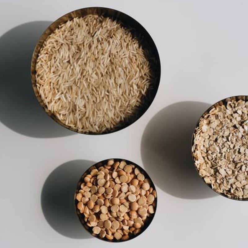 Aerial view of dry grains and cereals, including rice, lentils, and oats, arranged in bowls.