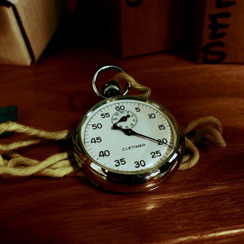 Close-up of an antique silver stopwatch resting on a wooden table with a yellow rope.