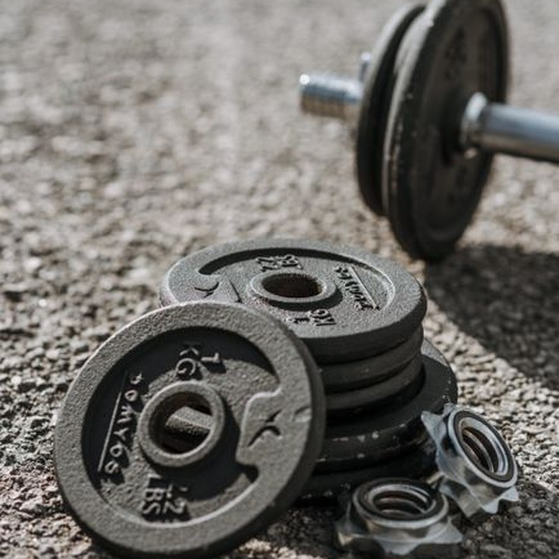 Adjustable dumbbells with weight discs left on asphalt sports ground in bright sunlight