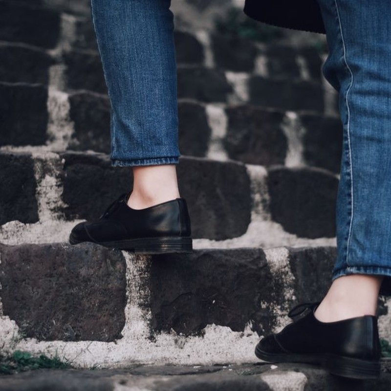 Person in denim jeans climbing stone stairs wearing black leather shoes.