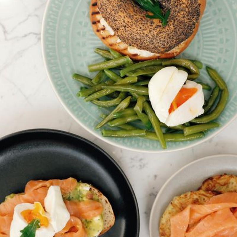 Various ceramic plates with tasty burger with asparagus and boiled egg and sandwiches with fish served on white marble table in modern kitchen