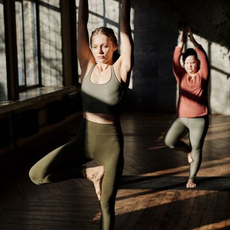 Two women practicing yoga in a serene sunlit room, focusing on balance and flexibility.