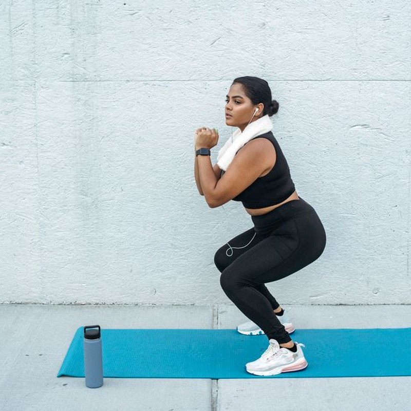 Confident woman doing squats on a yoga mat with a water bottle nearby. Fitness and lifestyle concept.
