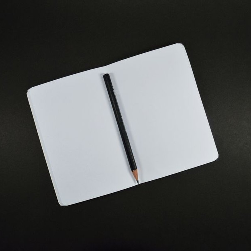 Top view of an open blank notebook with a pencil on a black background, perfect for creative projects.