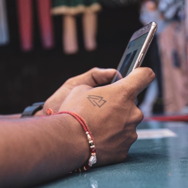 Detailed view of a hand with a tattoo holding a smartphone indoors, showcasing modern technology.