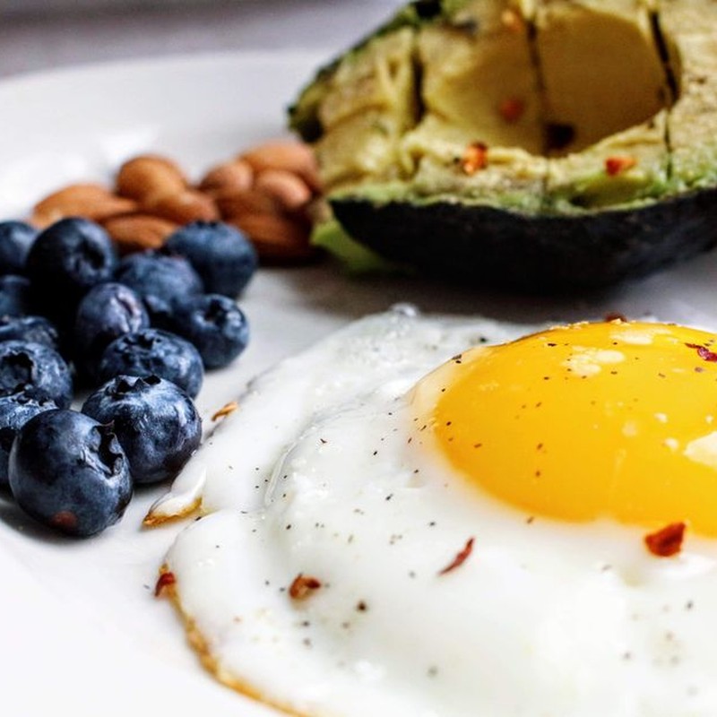A nutritious breakfast featuring a fried egg, avocado, blueberries, and almonds.