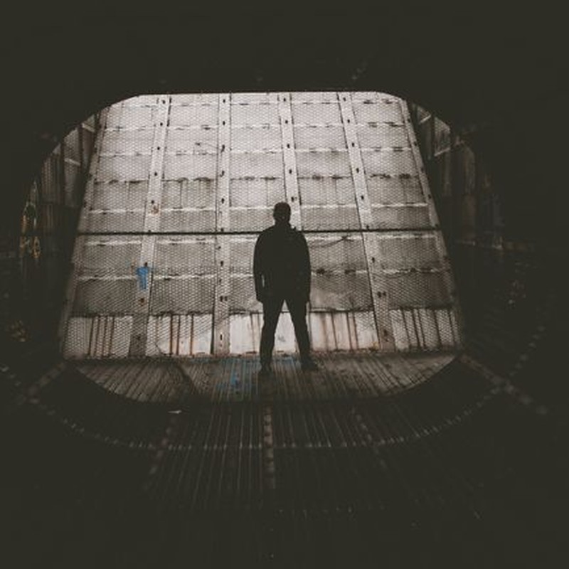 Moody silhouette of a person standing inside a dimly lit industrial tunnel.