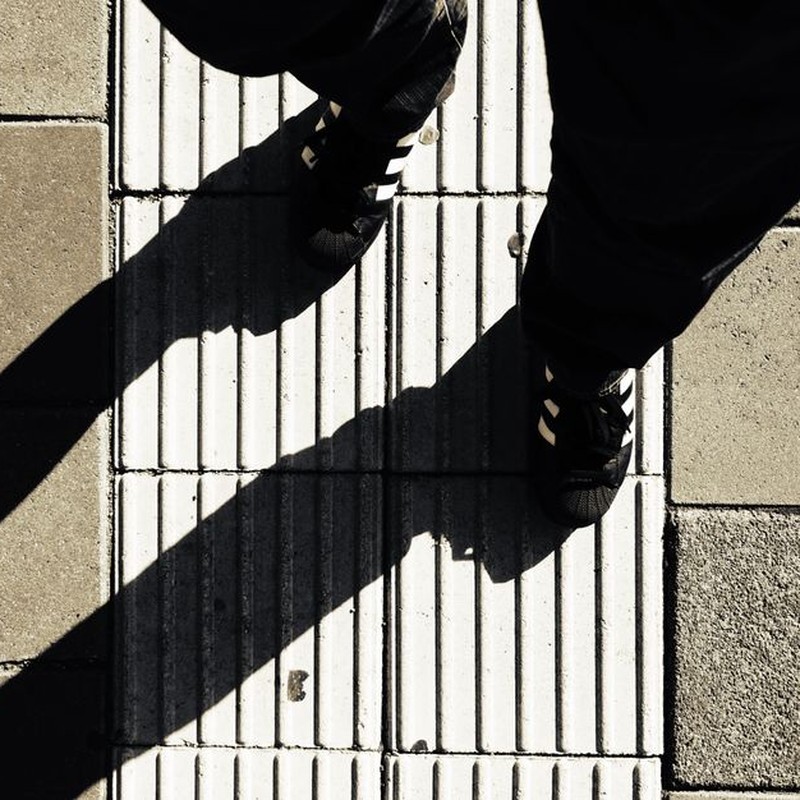 Striking shadows cast by feet on a textured urban pavement in daylight.
