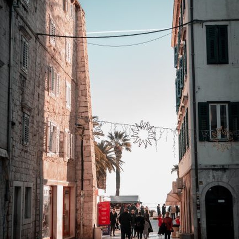 A bustling pedestrian walkway in Split, Croatia, featuring historic stone buildings and palm trees under a clear sky.