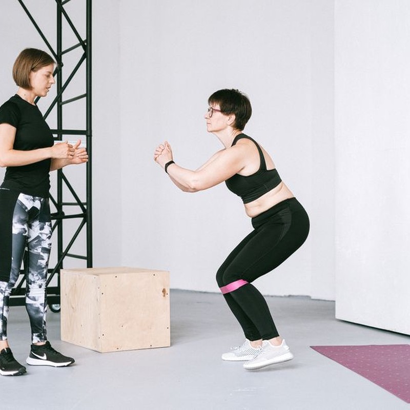 Two women engaging in a fitness workout with resistance bands at an indoor gym.