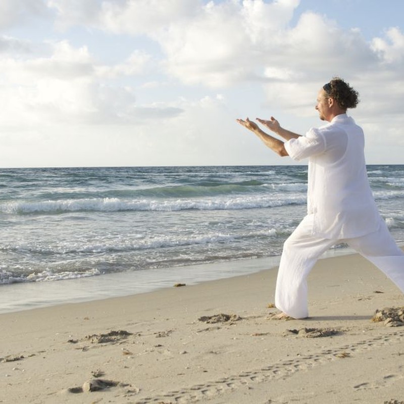 A serene scene of a man practicing Tai Chi on a quiet beach with gentle waves.