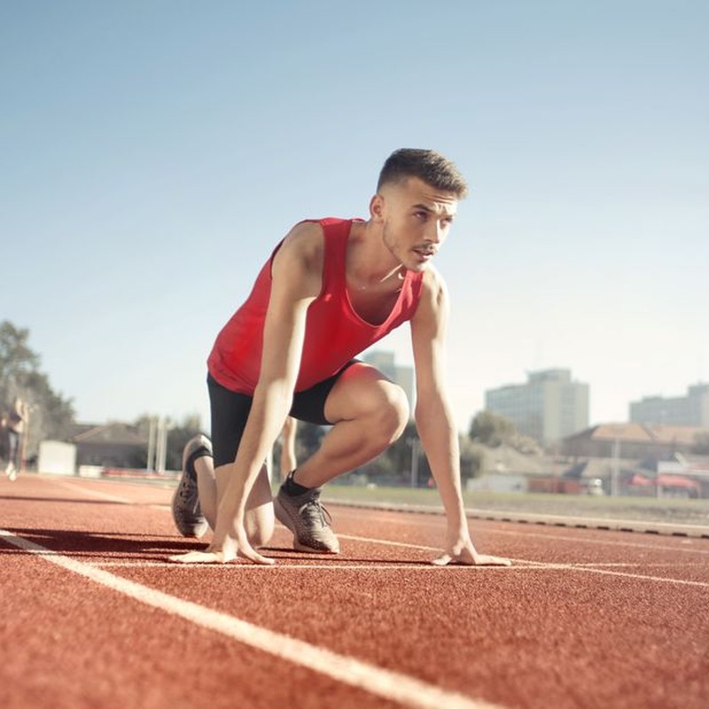Young male athlete in start position on outdoor track, ready to sprint.