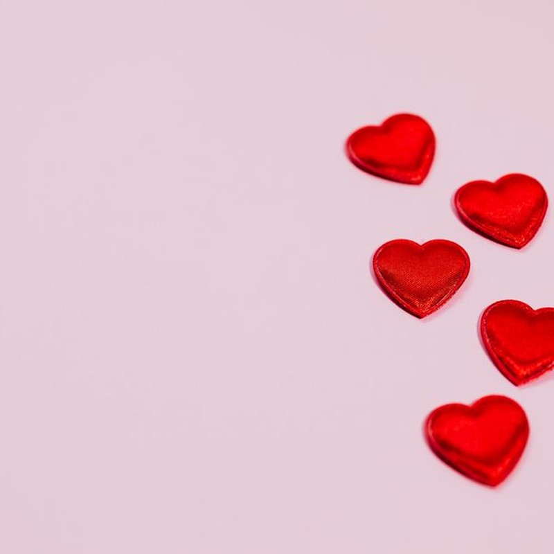 Five red heart shapes on a pastel pink background, ideal for Valentine's Day themes.