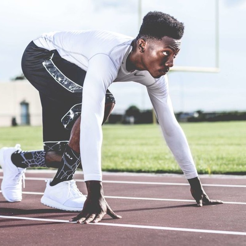 Focused athlete in starting position on a sunny track field, ready to sprint.
