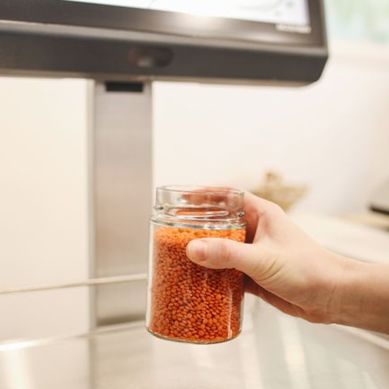 Hand holding a jar of red lentils on a digital weighing scale in an eco-friendly store.