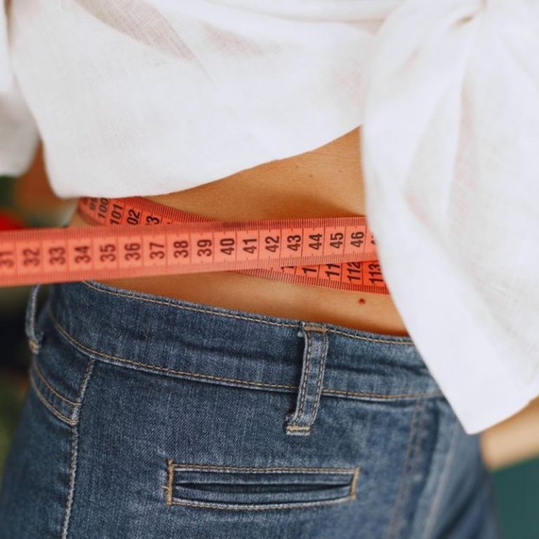 Close-up image of a woman measuring her waist with a tape measure, promoting fitness and health goals.