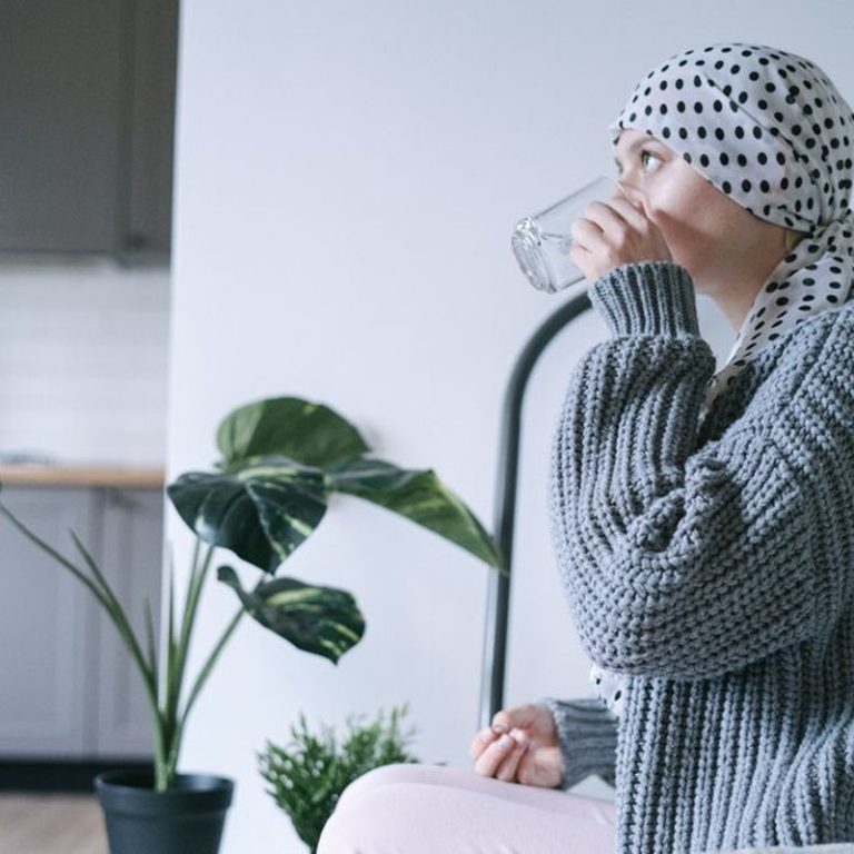 A woman wearing a headscarf drinks water indoors, promoting recovery and wellness.