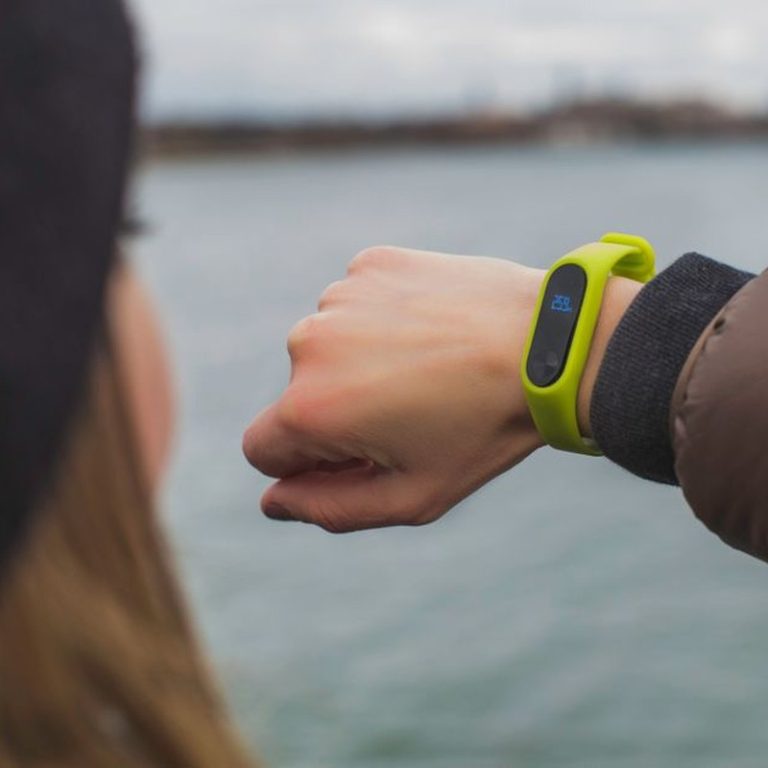 Close-up of a woman outdoors checking the time on her smartwatch by a lake.