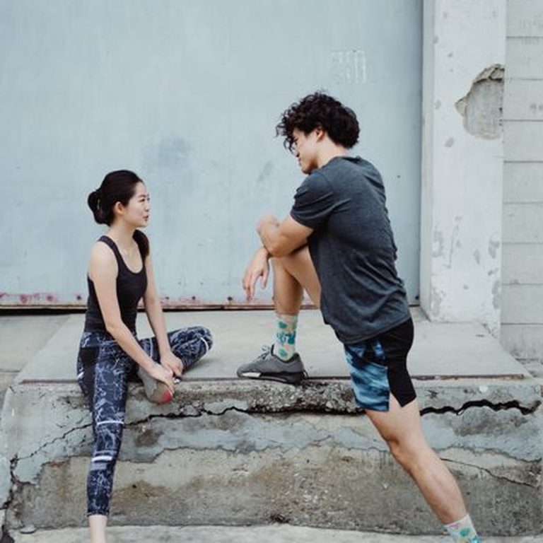 Two athletes stretching and warming up on a concrete sidewalk for exercise.