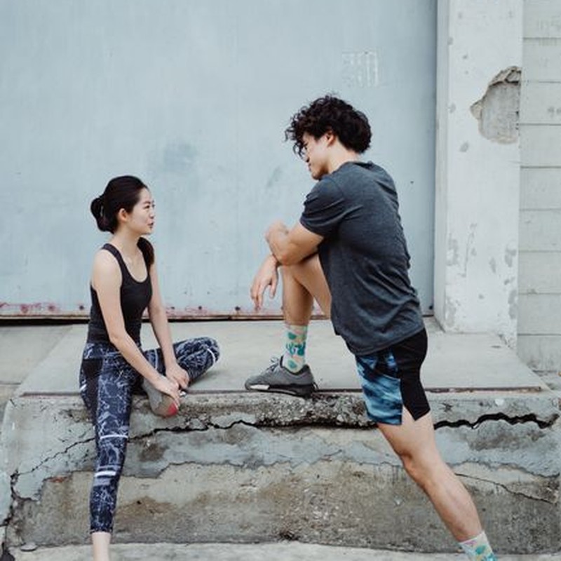 Two athletes stretching and warming up on a concrete sidewalk for exercise.