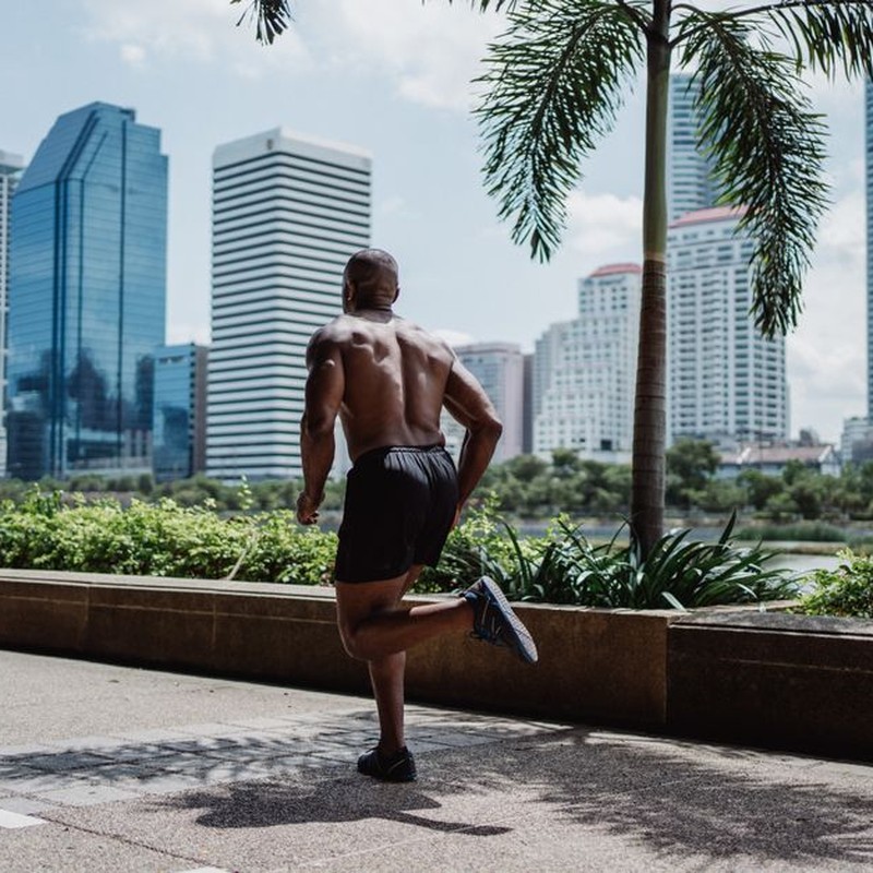 Shirtless man jogging in city park with skyscrapers in the background. Fitness and urban lifestyle concept.