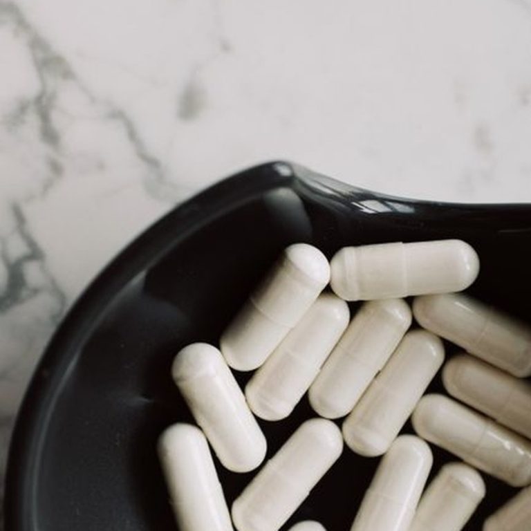 A close-up view of white capsules in a black bowl on a marble surface, emphasizing medicine and health.