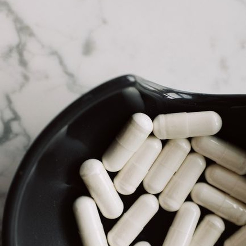 A close-up view of white capsules in a black bowl on a marble surface, emphasizing medicine and health.