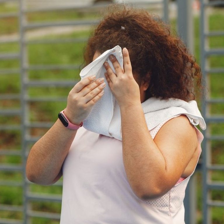 Woman wipes sweat after outdoor workout in summer sun, showing fitness and resilience.