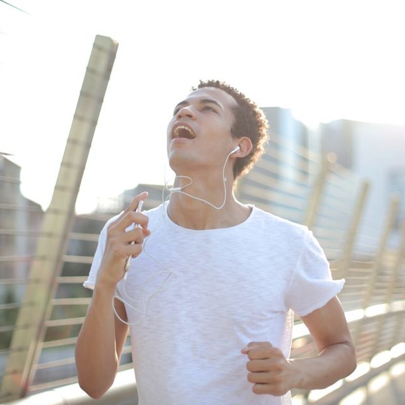 A young man running outdoors on a sunny day, enjoying music through earbuds.