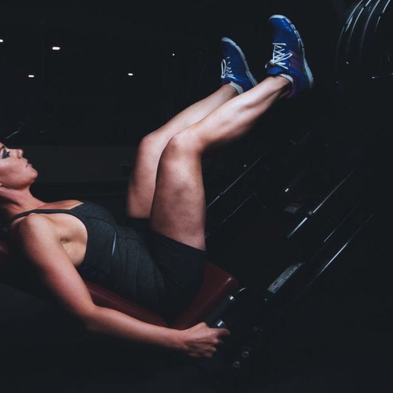 Focused woman doing leg press exercise in a dimly lit gym.