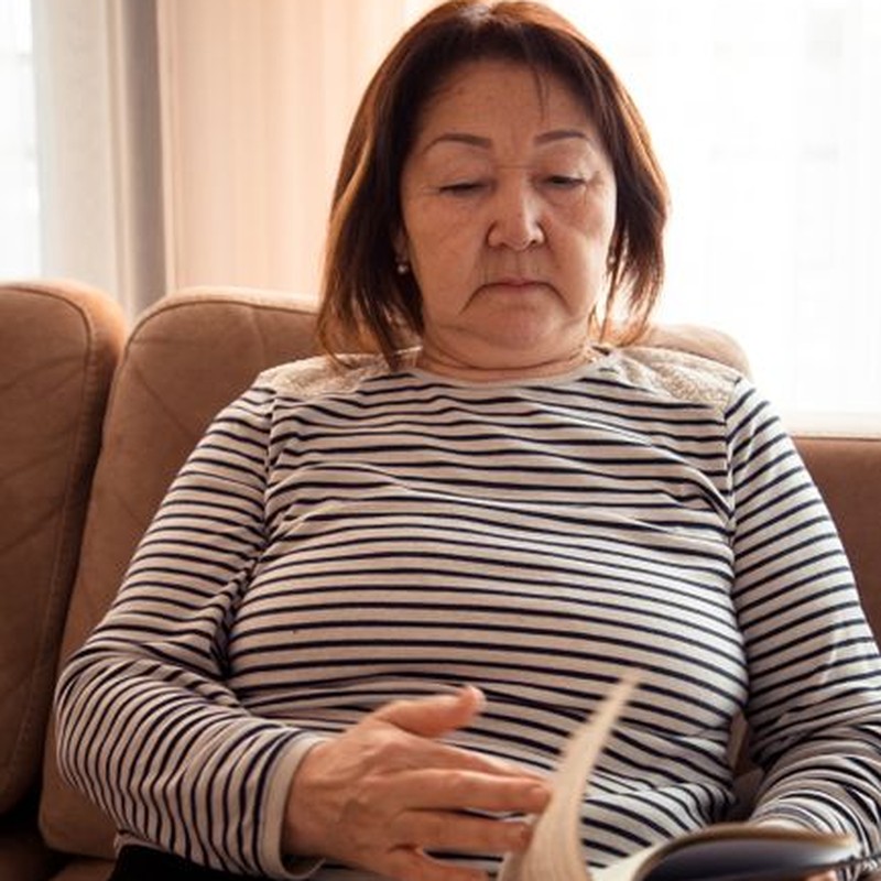 Middle aged ethnic focused female looking through interesting novel on sofa of lounge in daytime