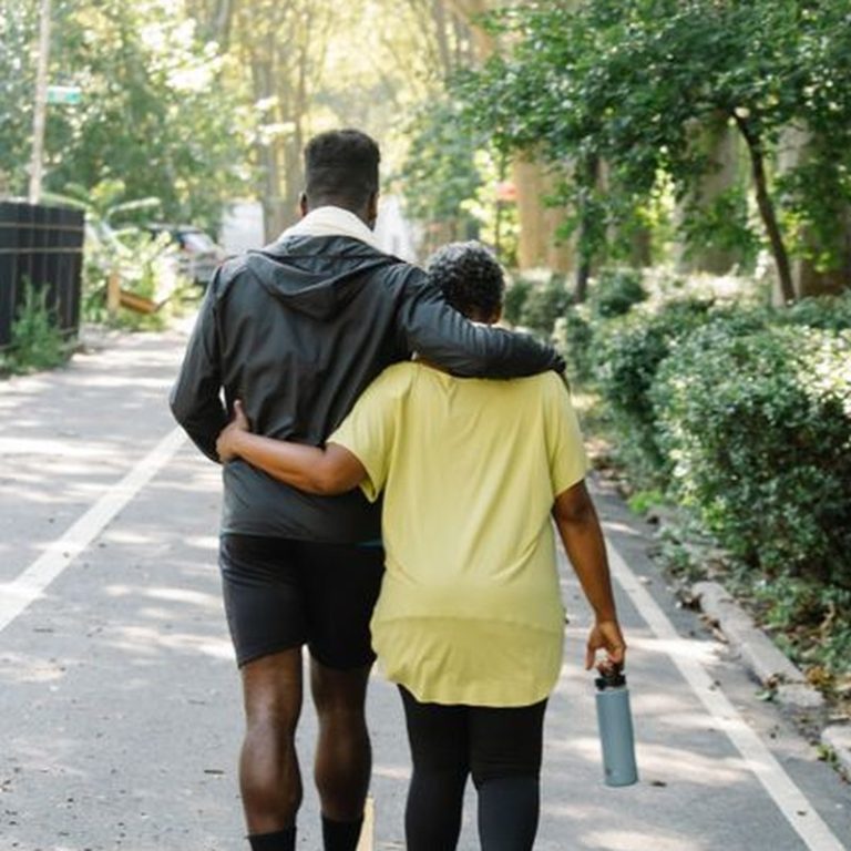 A couple walking together down a tree-lined path, embodying a healthy and active lifestyle.