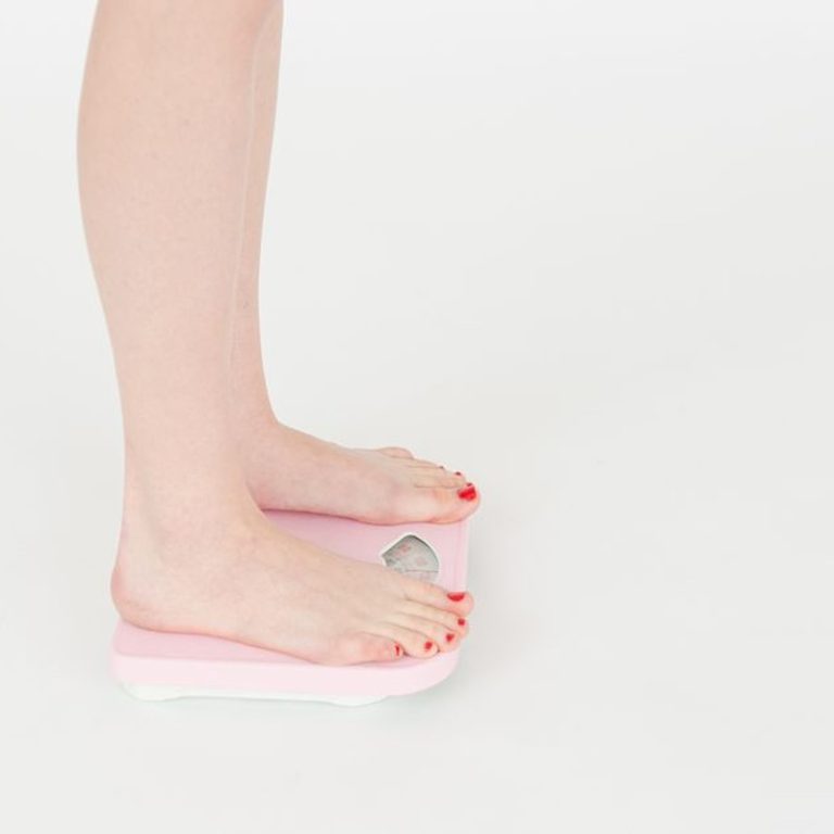 High angle side view of crop faceless female standing on scales and measuring weight on white background