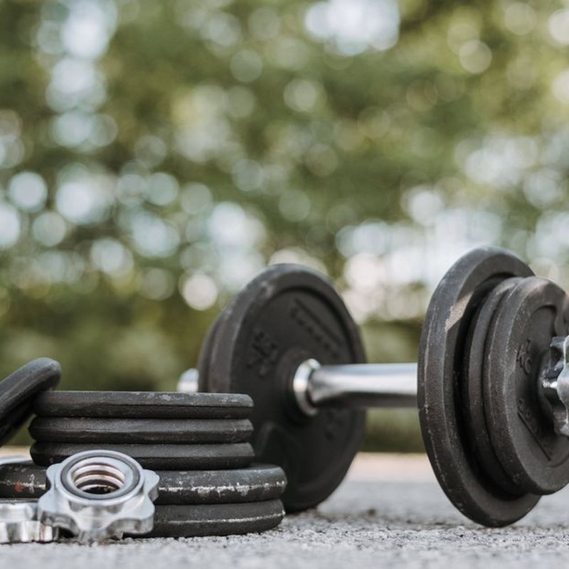 Ground level of adjustable dumbbell on stainless steel bar near plates and screw collars on rough walkway on street