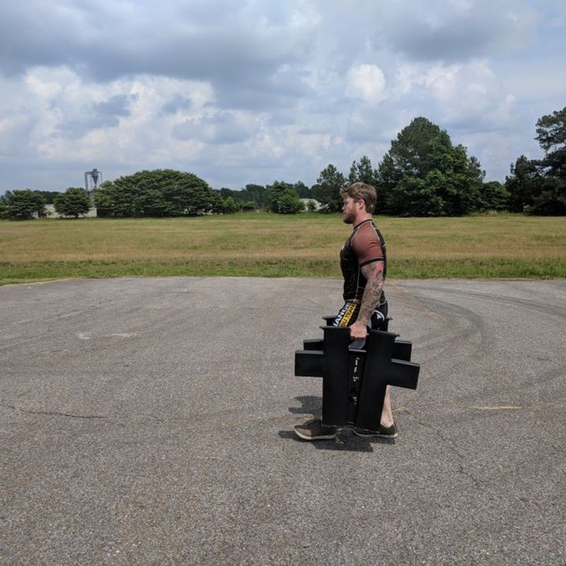 A man participates in strength training by walking outdoors with heavy weights on a clear day.