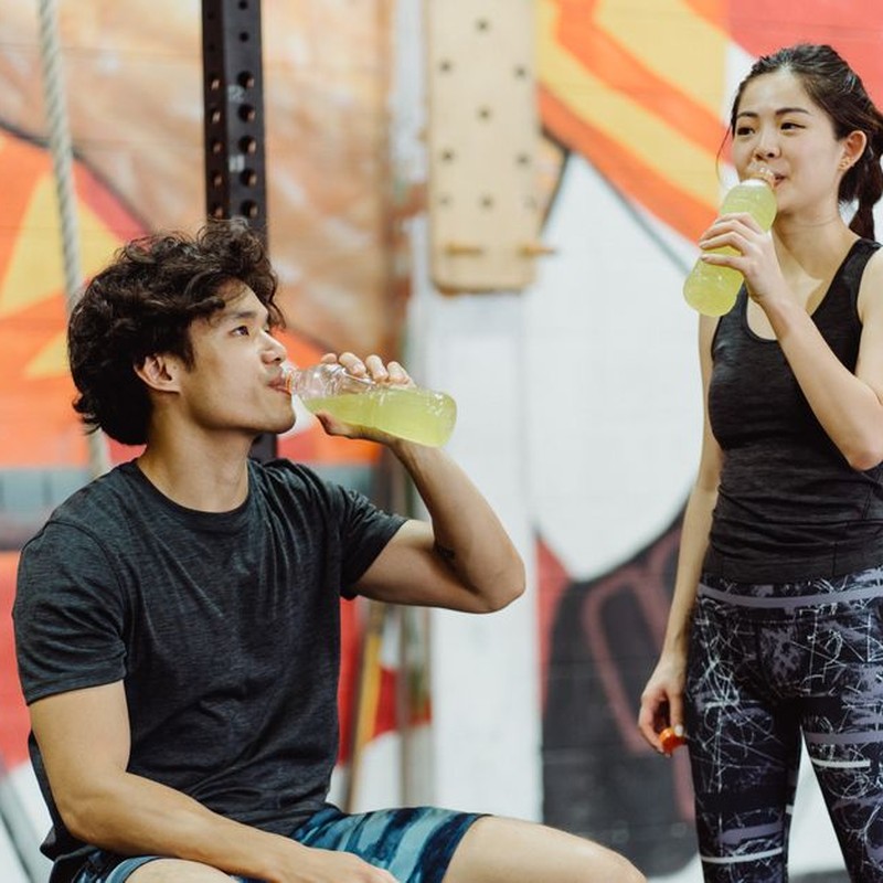 Asian couple in gym attire drinking energy drinks after workout. Vibrant and lively setting.