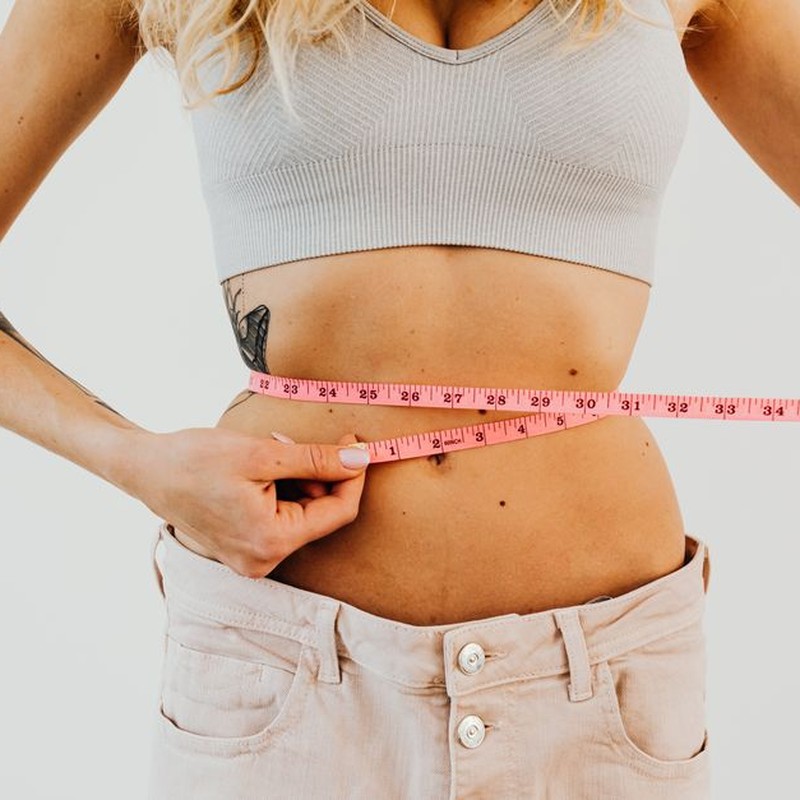 Close-up of woman in sports bra measuring waist with pink tape for fitness goals.