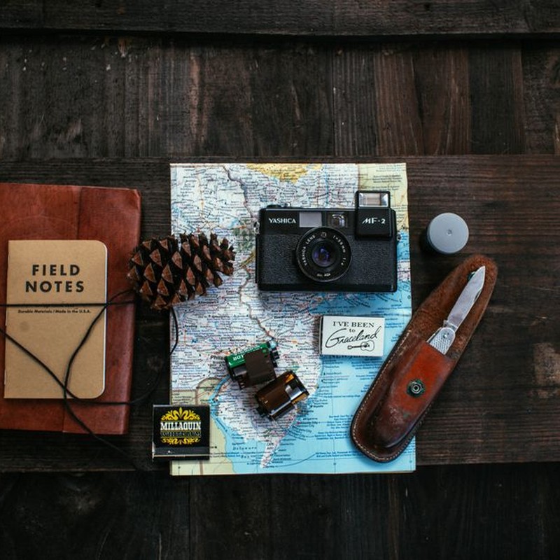 Overhead of retro photo camera near bump and films near notepad and map on wooden surface