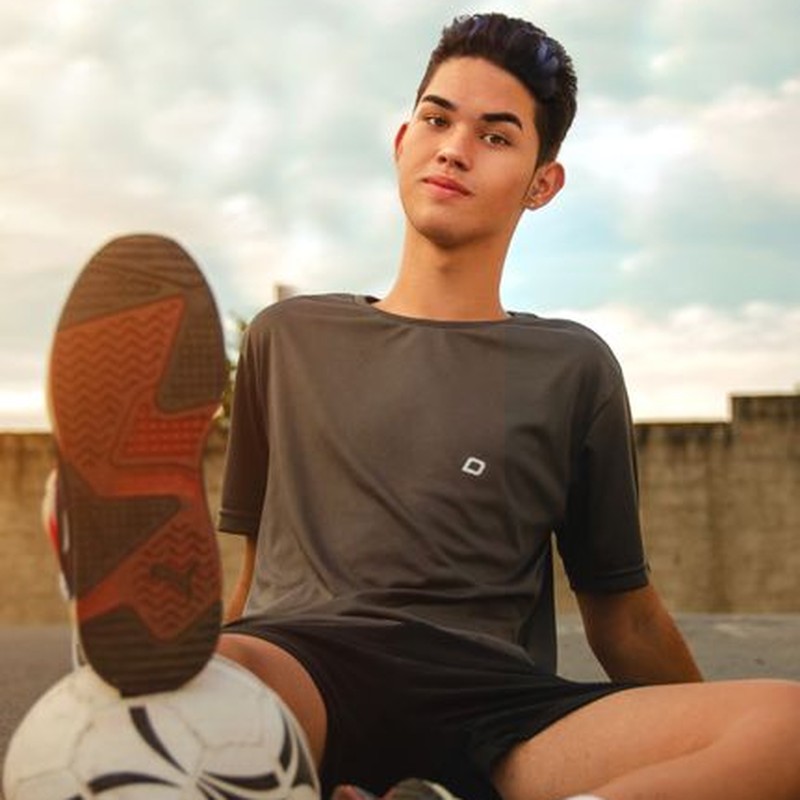 Young male soccer player sitting outdoors with a soccer ball, confident and relaxed.