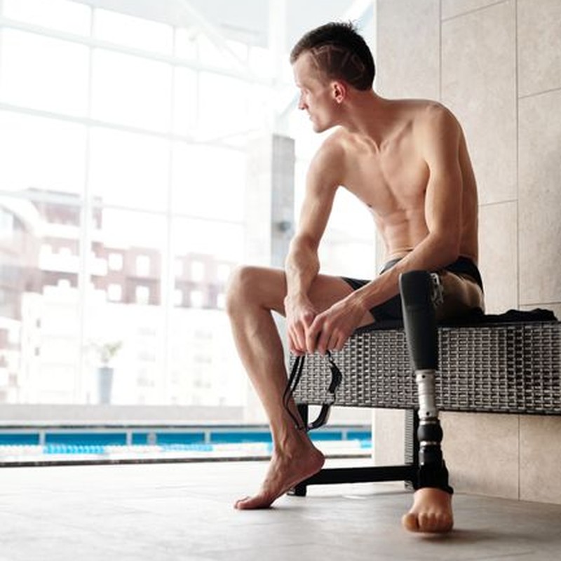 Young man with a prosthetic leg sitting by an indoor swimming pool.