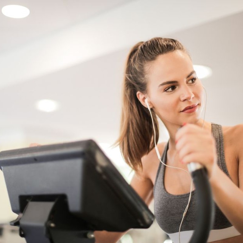 Fit woman working out on an elliptical machine indoors, wearing headphones and a sports bra.
