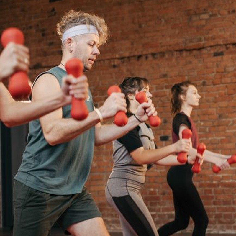 Diverse group exercising with dumbbells in an indoor gym setting, promoting healthy lifestyle.