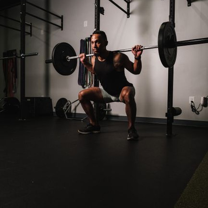 Muscular man performing squats with weights in gym, showcasing strength and fitness.