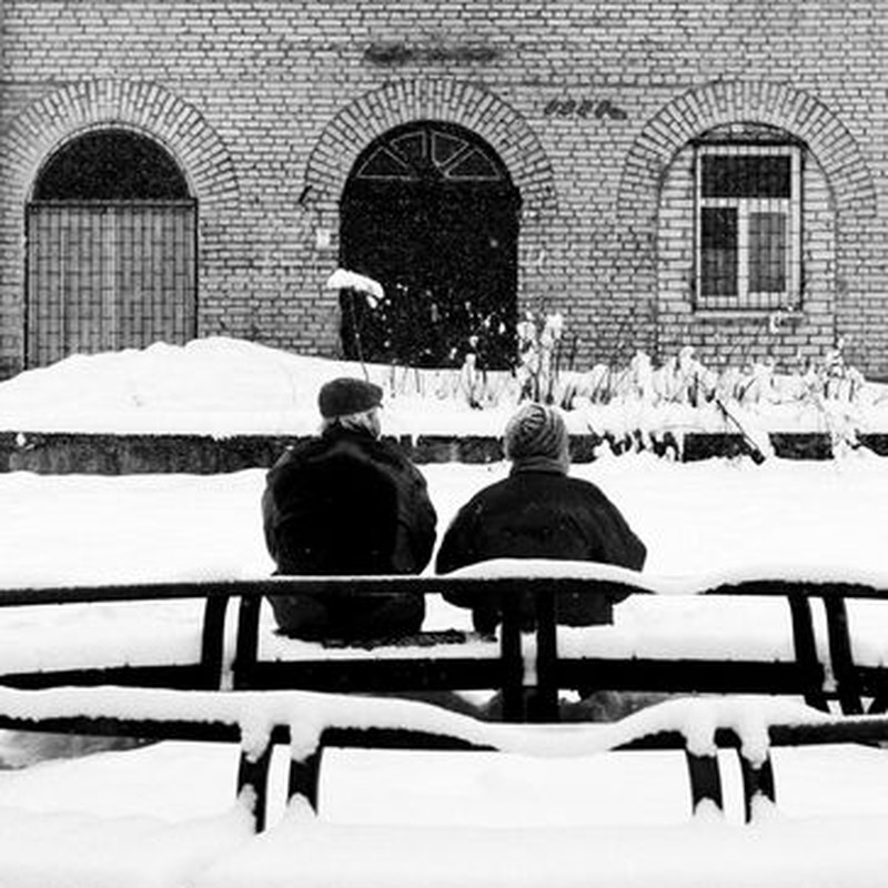Two adults seated on a snowy street in Minsk, Belarus, during winter.