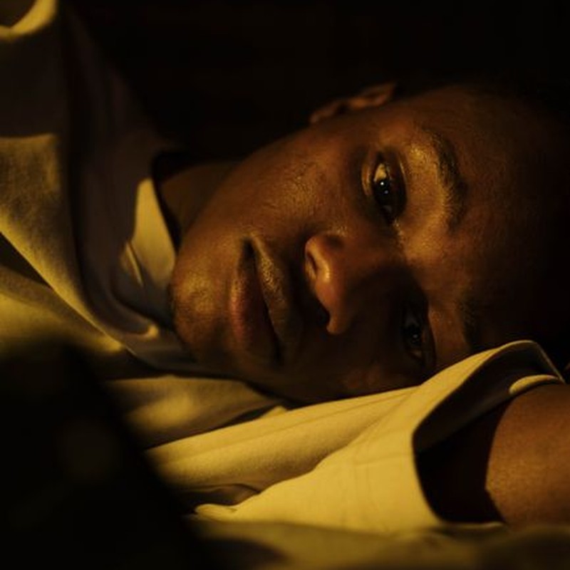 A young man lying awake in bed, depicting insomnia and sleeplessness.