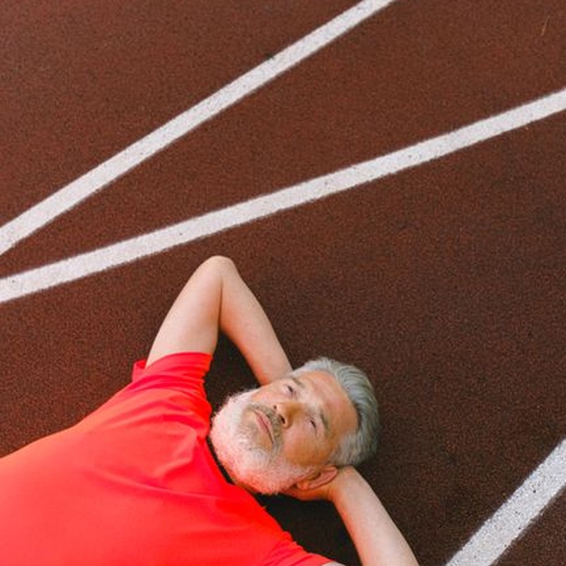 Senior man in red shirt lying relaxed on a running track outdoors, showcasing mental calmness.