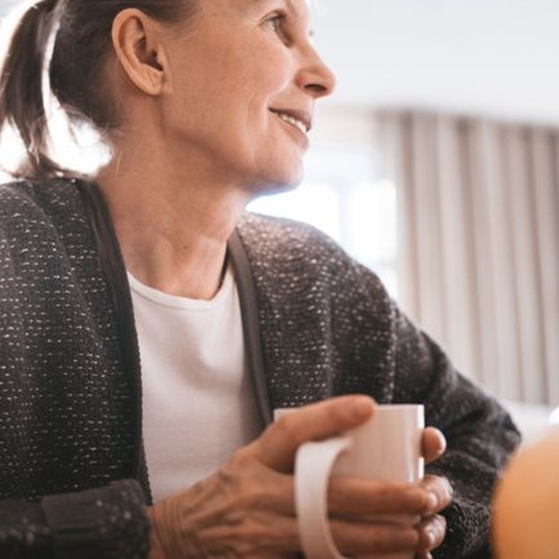 Senior woman holding a mug, smiling and enjoying a warm drink indoors.