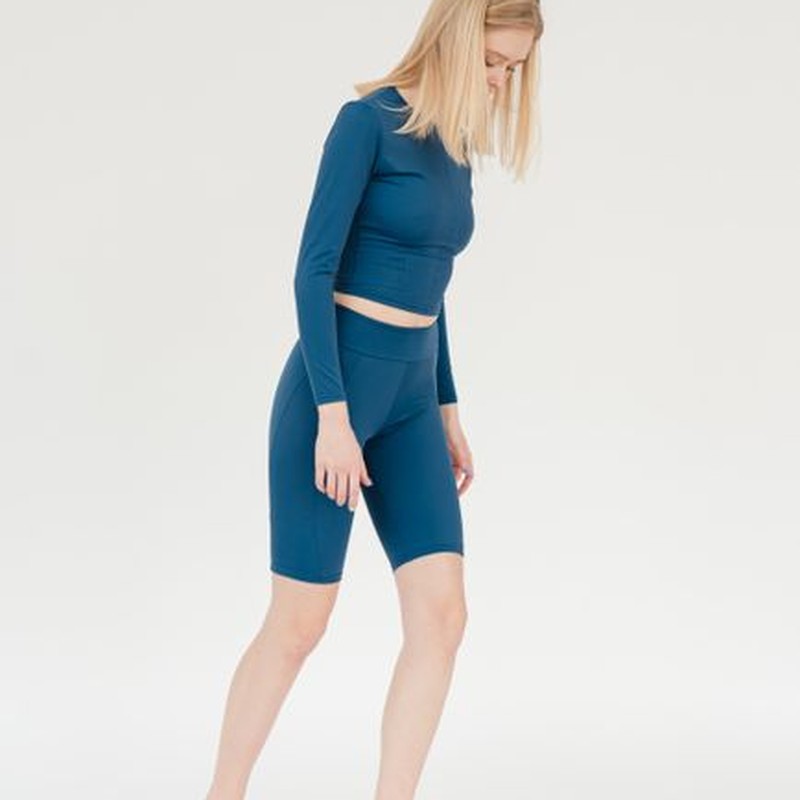 Full body of slender female in sportswear checking weight on scales in studio against white background